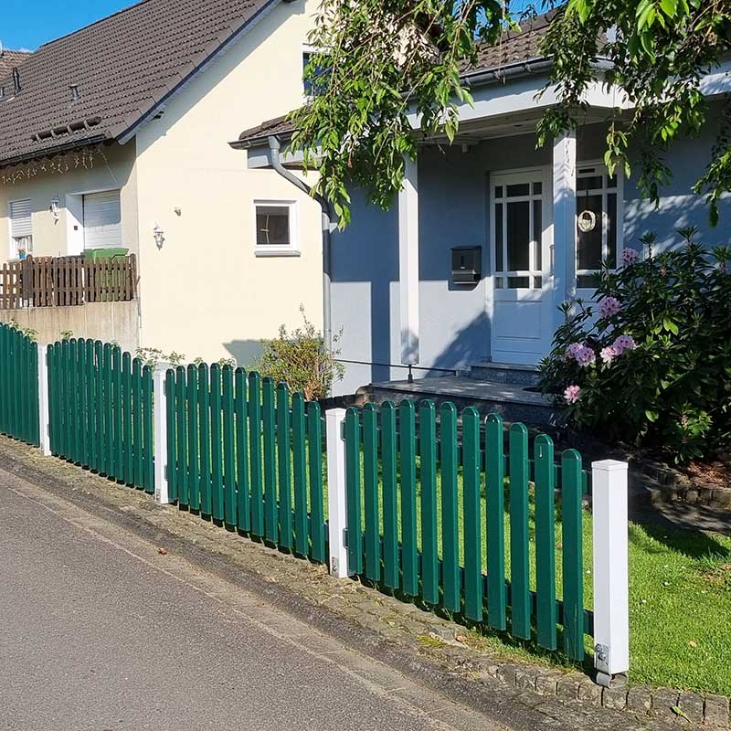 Lattenzaun in weiß und moosgrün als Wellenform im Hintergarten